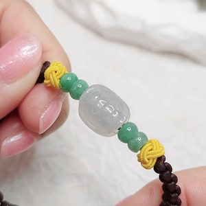 Peut inclure: Un bracelet en jade avec une perle de jade vert clair, deux n&oelig;uds jaunes et une cordelette brune. Le bracelet est nou&eacute;.