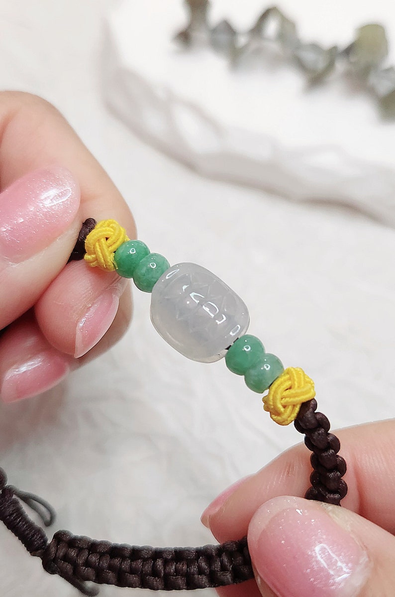 Peut inclure: Un bracelet en jade avec une perle de jade vert clair, deux n&oelig;uds jaunes et une cordelette brune. Le bracelet est nou&eacute;.