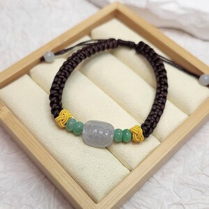 Peut inclure: Un bracelet tress&eacute; marron avec un charme en perles de jade vert et jaune. Le bracelet est pr&eacute;sent&eacute; dans une bo&icirc;te en bois.