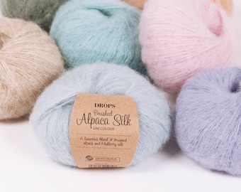 May include: A collection of yarn balls in various pastel colors, including light green, light blue, pink, and beige. The yarn is labeled "DROPS Brushed Alpaca Silk UNI COLOUR" and describes it as a luxurious blend of brushed alpaca and mulberry silk.