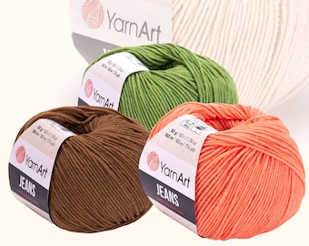 May include: Four balls of YarnArt Jeans yarn in white, green, brown, and orange. Each ball is labeled with the brand name, yarn weight, and yardage.