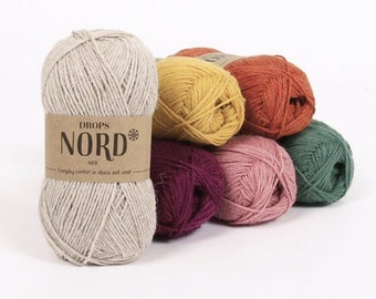 Könnte beinhalten: Eine Sammlung von Wollknäuel in verschiedenen Farben, darunter Beige, Gelb, Orange, Grün, Rosa und Burgunderrot. Das Garn ist mit "DROPS NORD MIX" gekennzeichnet und trägt den Schriftzug "Alltagskomfort aus Alpaka und Wolle".