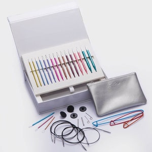 Peut inclure: Un ensemble d'aiguilles à tricoter interchangeables colorées dans une boîte blanche avec une pochette argentée portant l'inscription "KnitPro". L'ensemble comprend des aiguilles de différentes tailles, un câble, des marqueurs de mailles et d'autres accessoires.