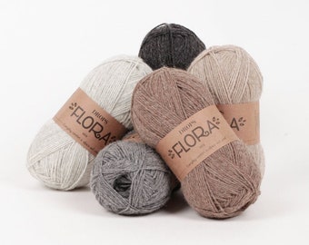 Puede incluir: Cuatro ovillos de hilo Drops Flora en diferentes colores: beige, marrón claro, gris y gris oscuro. Cada ovillo tiene una etiqueta marrón con el texto "DROPS FLORA" y "Simply comfort in alpaca and wool."