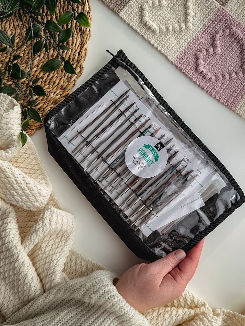 May include: A set of interchangeable knitting needles in a clear plastic case with a black zipper. The case has a label that says "Dyakcraft Pro Romance Interchangeable Knitting Needles".