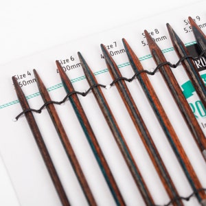 May include: A set of eight double-pointed knitting needles in various sizes, ranging from 4.00 mm to 5.5 mm. The needles are made of wood and have a dark brown and blue striped pattern.