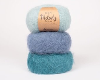 Puede incluir: Tres ovillos de hilo Drops Melody en tonos azules y verde azulado. La etiqueta dice "Drops Melody Uni Colour Una mezcla lujosa de lana y alpaca."