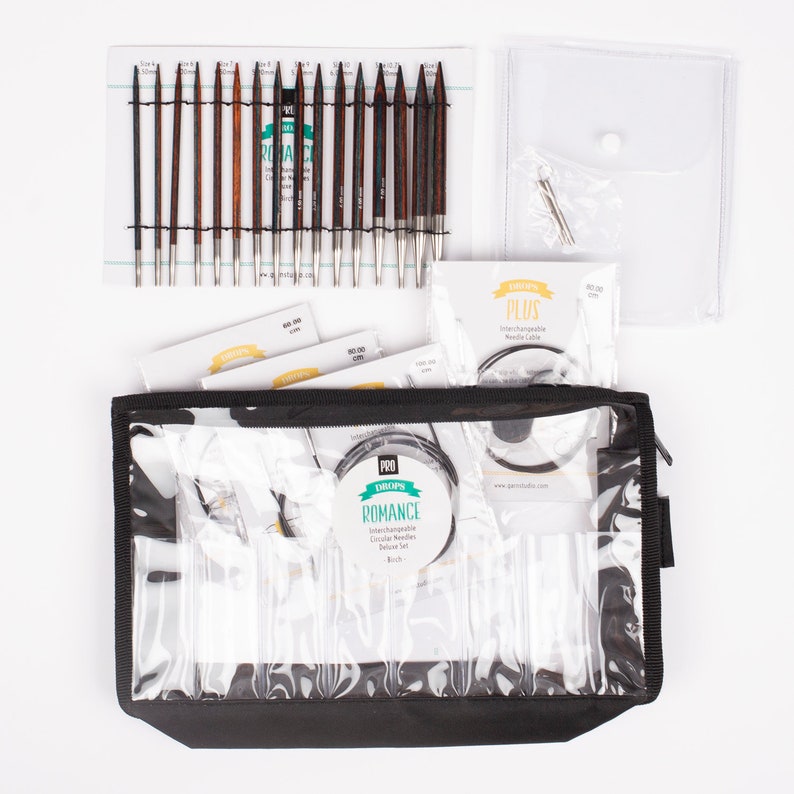May include: A set of interchangeable circular knitting needles in a black zippered case. The needles are made of wood and have a silver metal tip. The set includes a variety of sizes, from 2.5 mm to 8 mm. The case also includes a needle gauge and a set of cable connectors. The set is labeled "DROPS Romance Interchangeable Circular Needles Deluxe Set - Birch".