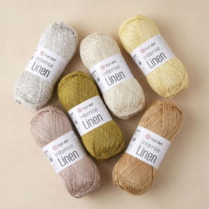 May include: A collection of seven skeins of YarnArt Intense Linen yarn in various colors. The yarn is labeled with the brand name and "Linen". Colors include light grey, cream, yellow, olive green, mauve, and tan. The skeins are arranged on a neutral background.