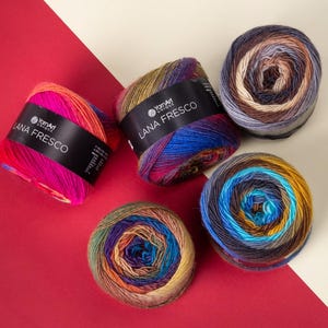 May include: A top-down shot displays five colorful yarn skeins on a red and cream background. The yarn is labeled "Lana Fresco" and features a variety of colors, including pink, orange, blue, green, and brown. The yarn is arranged in a visually appealing pattern.