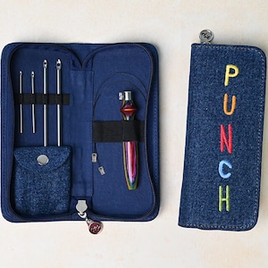 May include: A blue denim case with a zipper closure, containing a set of knitting needles and a colourful wooden punch needle. The case has a small pocket on the front and the word "PUNCH" is embroidered on the side of the case in rainbow colours.