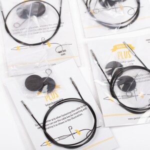 May include: Close-up of a set of black interchangeable knitting needles with a cable key. The needles are packaged in clear plastic bags with white labels that say "DROL PLUS Interchangeable Needle Cable".
