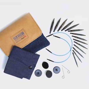 May include: A set of 15 interchangeable circular knitting needles in a denim-themed case. The needles are black with gold tips and come with blue cords and black end caps. The case is made of brown faux leather with a blue denim lining and features the text "DENIM SPECIAL COLLECTORS EDITION by Knit Pro".