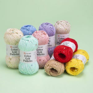 Può includere: Una collezione di gomitoli di lana colorati in varie tonalità, tra cui crema, blu, viola, rosa, rosso, giallo e marrone. Ogni gomitolo è etichettato "Cotton Gold Paillettes" e decorato con paillettes. Ideale per progetti di maglia e uncinetto.