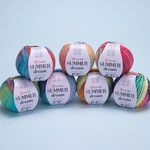 Peut inclure: Sept pelotes de laine YarnArt Summer Dream multicolores sont présentées. Chaque pelote porte une étiquette avec le texte "SUMMER dream" et le logo YarnArt. Les couleurs de la laine comprennent le bleu, le vert, le rose, le jaune et l'orange.