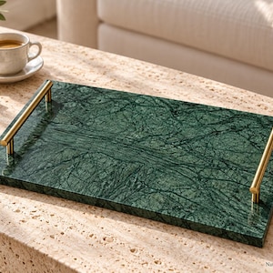May include: A rectangular green marble serving tray featuring a polished surface with dark natural veining and two brushed gold metal handles attached to the sides. The tray has a flat base and a smooth, glossy finish throughout the stone.