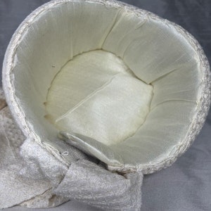 Pode incluir: Um chap&eacute;u branco de croch&ecirc; com forro de cetim branco. O chap&eacute;u tem uma aba larga e um la&ccedil;o de lado.