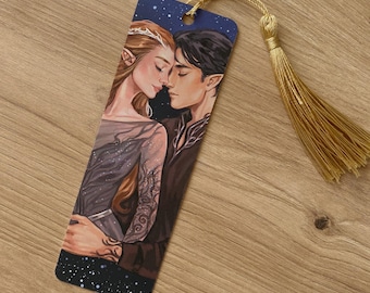 May include: A bookmark featuring a romantic illustration of a couple embracing. The artwork depicts a woman with long auburn hair and a man with dark hair, set against a starry night sky. A gold tassel hangs from the top.