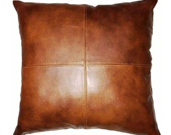 May include: A square throw pillow in a rich, medium-brown color with a smooth, uniform texture. The pillow features a distinct cross-shaped seam pattern that divides the front surface into four equal quadrants, with visible stitching along the lines.