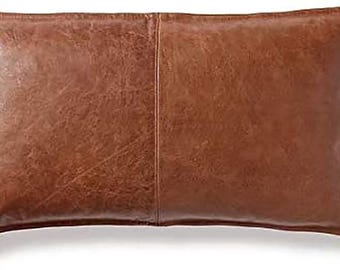 Puede incluir: Una almohada de cuero marrón con una costura en el centro. La almohada es rectangular y tiene un borde ligeramente redondeado.