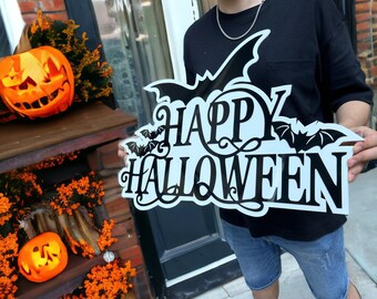 May include: A person holding a white sign with black lettering that says "Happy Halloween" with bats on either side of the text. The sign is decorated with a black and white swirl design.