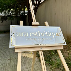May include: A white sign with gold lettering on an easel. The sign reads "cara esth&eacute;tique. CENTRE DE BEAUTE."