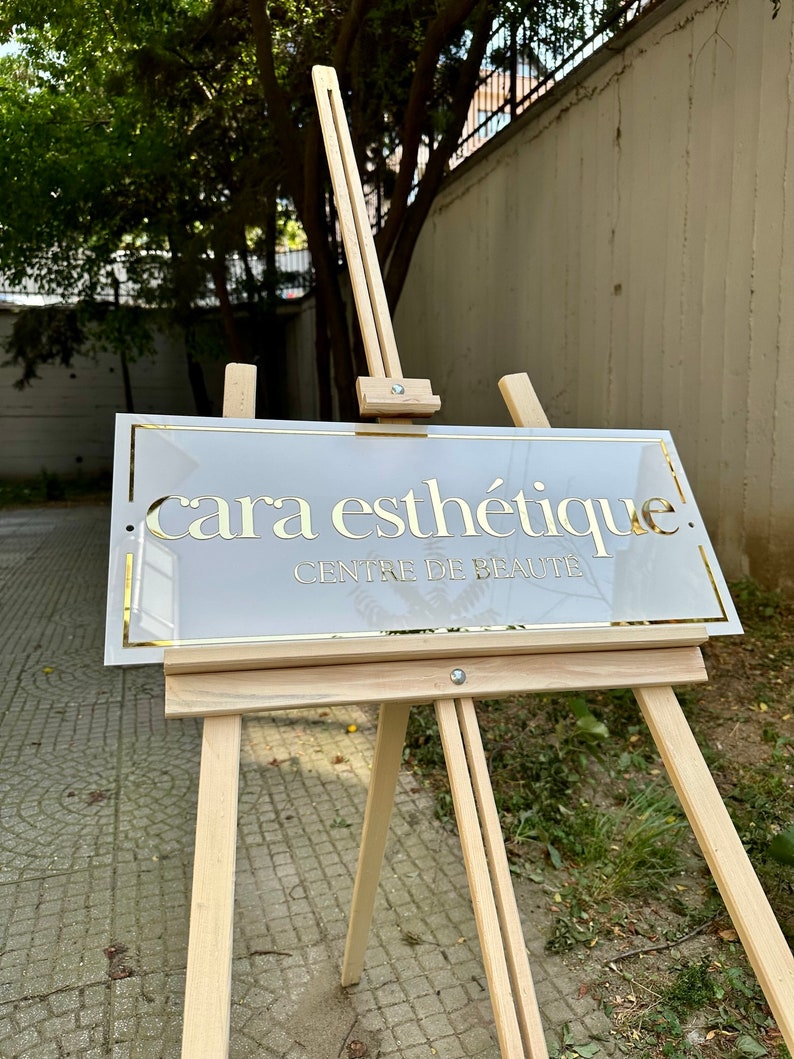 May include: A white sign with gold lettering on an easel. The sign reads "cara esth&eacute;tique. CENTRE DE BEAUTE."