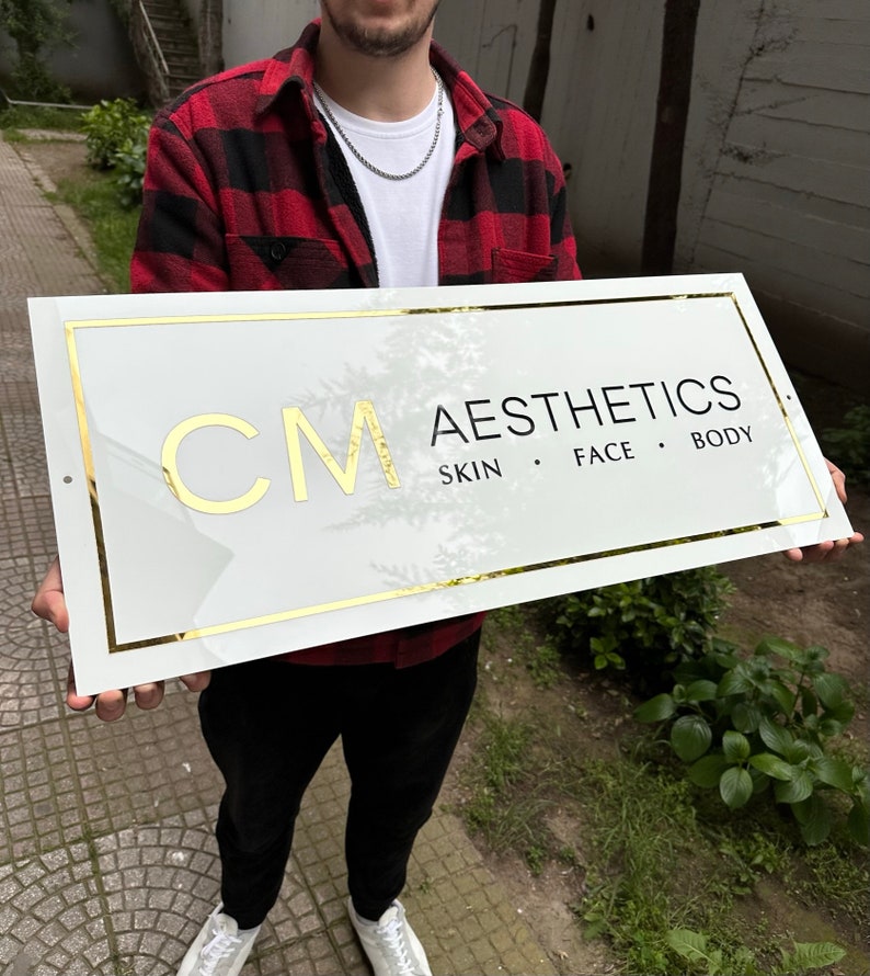 May include: White sign with gold trim and black text. The sign reads "CM AESTHETICS SKIN FACE BODY".