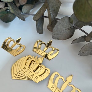 May include: Gold mirror crown with the name "BITAR" engraved on it. The crown is a popular party decoration for a birthday or special event.
