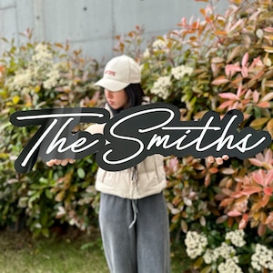 以下が含まれることがあります： 「The Smiths」と白文字で書かれた黒い看板を持っている人