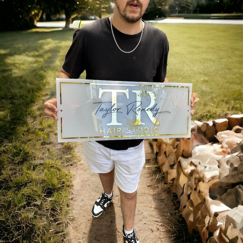May include: A white sign with gold lettering that reads "TR Taylor Romedy Hair Studio".
