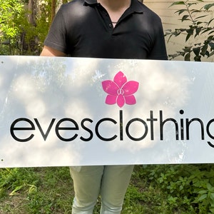 May include: A white sign with black text that reads "evesclothing" and a pink flower graphic.