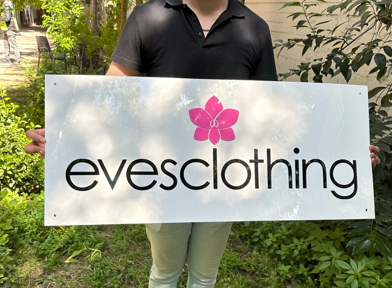 May include: A white sign with black text that reads "evesclothing" and a pink flower graphic.