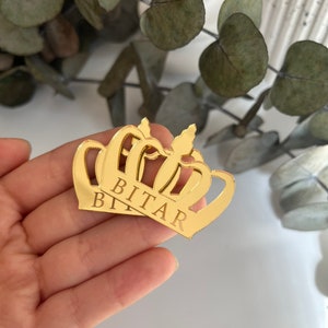May include: Gold mirror crown with the name "BITAR" engraved on it.