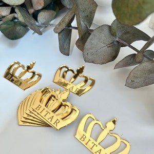 May include: Gold crown-shaped acrylic ornaments with the name "BITAR" engraved on each. The ornaments are perfect for adding a touch of elegance to any occasion.
