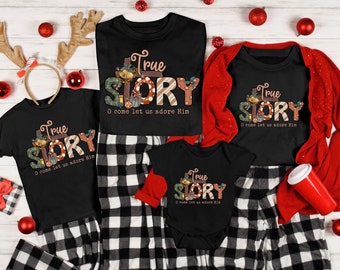 May include: A set of four black t-shirts with a Christmas-themed design. The shirts feature the words "True Story" with a festive illustration of a Christmas tree, presents, and ornaments. The text "O come let us adore Him" is also included on each shirt.