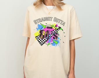 May include: A cream colored t-shirt with a graphic print that says "Straight Outta The 80's" with a colorful design of paint splatters and a checkered flag.