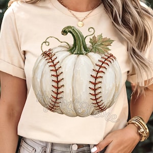 May include: A cream-colored short-sleeve t-shirt featuring a graphic of a white pumpkin designed to look like a baseball, complete with red stitching, a green stem, and a small leaf. The shirt has a crew neckline and a casual, relaxed fit.