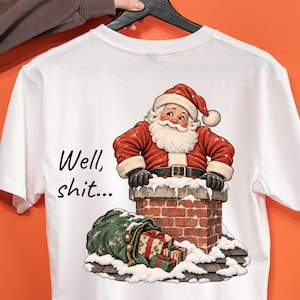Könnte beinhalten: Ein weißes T-Shirt mit einer Grafik vom Weihnachtsmann, der aus einem Backsteinkamin schaut, daneben ein grüner Geschenkesack auf einem verschneiten Dach. Der Text "Well, shit..." steht in schwarzer Schrift links neben dem Kamin.