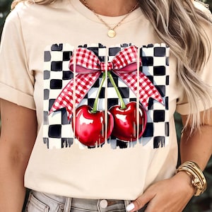 May include: A beige t-shirt featuring a checkered pattern and a red and white gingham bow with two red cherries on top.
