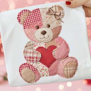 Könnte beinhalten: Ein weißer Stoff mit einem Patchwork-Teddybären-Design. Der Bär hat eine braune Nase, ein rotes Herz und eine Schleife. Der Patchwork-Stoff enthält verschiedene Muster in Rot-, Rosa- und Beigetönen.