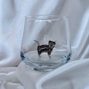 May include: A clear glass tumbler with a black glass cat figurine inside. The cat is sitting on the bottom of the glass.