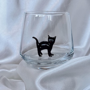 May include: A clear glass tumbler with a black glass cat figurine inside. The cat has black eyes and a white belly.