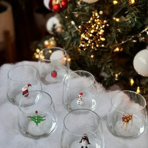Puede incluir: Seis vasos transparentes de vidrio con una variedad de adornos de vidrio con tem&aacute;tica navide&ntilde;a en su interior. Los adornos incluyen un mu&ntilde;eco de nieve, un &aacute;rbol de Navidad, un reno, un ping&uuml;ino, un Pap&aacute; Noel y un adorno rojo y blanco.