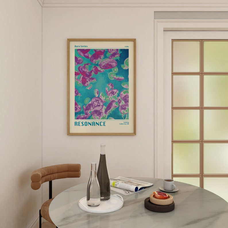 K&ouml;nnte beinhalten: Ein gerahmtes Poster mit einem blauen und violetten abstrakten Design von Quallen. Das Poster tr&auml;gt den Titel "RESONANCE" und ist Teil der "Rara Series". Das Poster h&auml;ngt an einer wei&szlig;en Wand &uuml;ber einem Tisch mit einer Glasflasche, einem Magazin und einem Teller mit Obst.