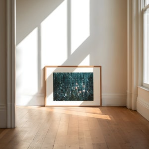 May include: A framed photograph of a green and blue abstract mosaic with pink accents. The photograph is hanging on a white wall in a room with hardwood floors.