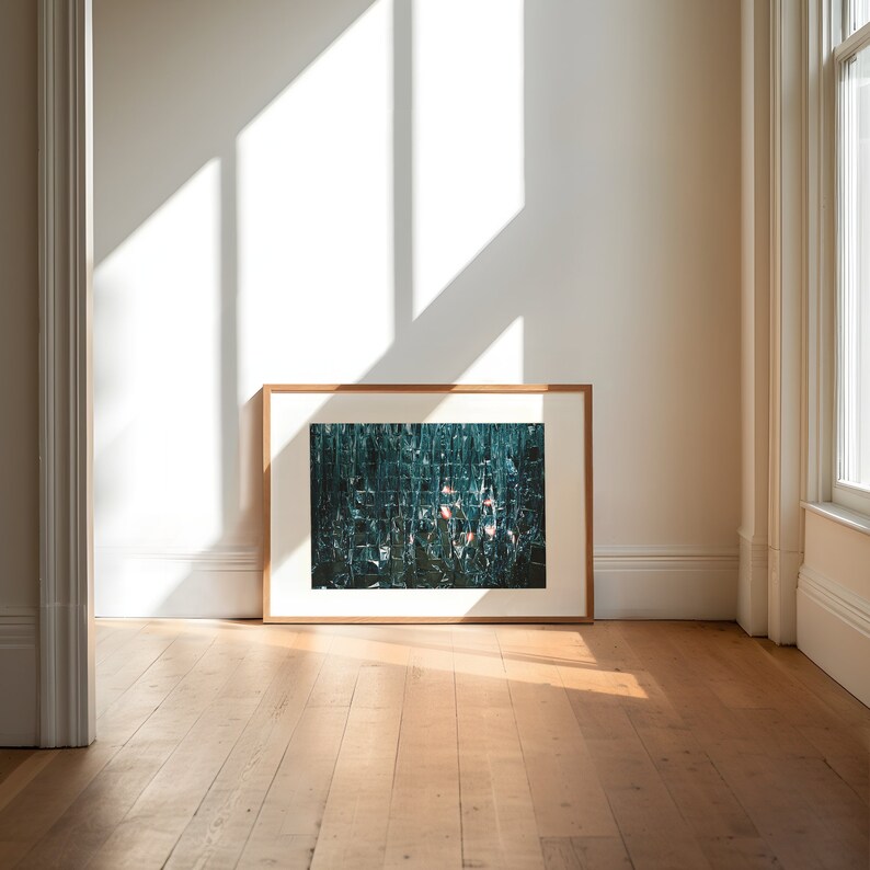 May include: A framed photograph of a green and blue abstract mosaic with pink accents. The photograph is hanging on a white wall in a room with hardwood floors.