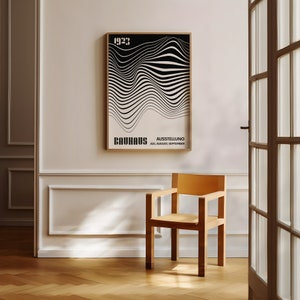Peut inclure: Une affiche noir et blanc avec un motif géométrique et le texte "1923 Bauhaus Ausstellung Jul. August. September" accrochée à un mur blanc dans une pièce avec une chaise en bois.