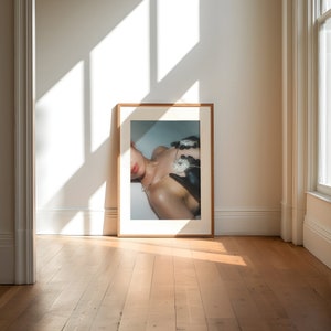 Op de afbeelding: Een ingelijste foto van een persoon die een zwart-wit gepatroneerd top draagt met een zilveren kettingketting. De persoon ligt met zijn hoofd naar de zijkant gedraaid.