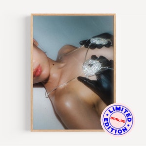 Op de afbeelding: Een close-up van de borst van een vrouw met een grote, met diamanten bezette ketting met hanger en zwarte handschoenen. De ketting heeft de vorm van een dollar-teken. De achtergrond is lichtblauw. De afbeelding heeft een "LIMITED EDITION ANALOG" stempel in de rechterbenedenhoek.